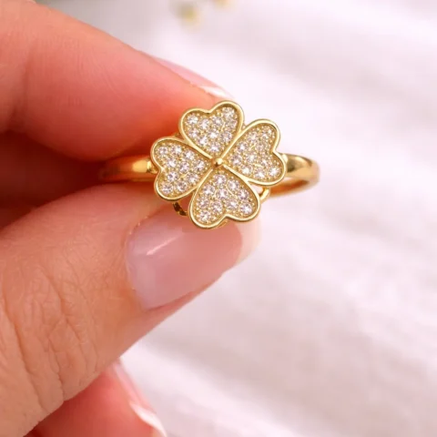 Anillo Aura Trébol dorado con circonitas sujeto entre los dedos