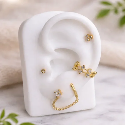 Piercing Nexa Bloom dorado colocado en la oreja con diseño floral de circonitas