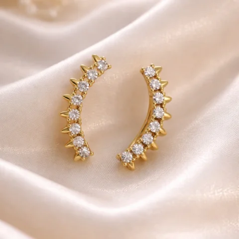 Pendientes trepadores Curve dorados con circonitas sobre fondo natural