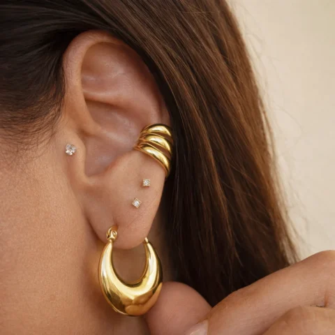 Pendientes Aros Nova dorados pequeños puestos en oreja con estilo minimalista