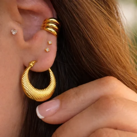 aros esencia dorados puestos en oreja con textura elegante