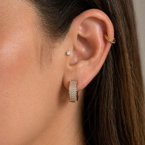Aros Éclat dorados en oreja de mujer con diseño pavé brillante y estilo elegante