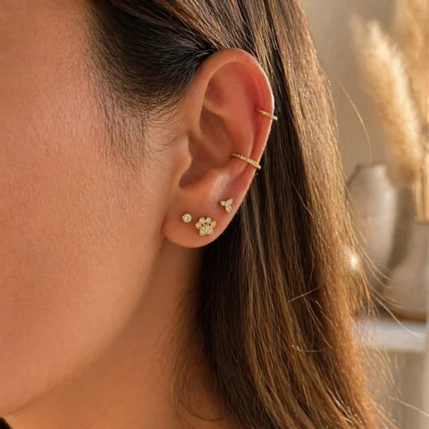 Piercing Nexa Paw dorado en oreja combinado con otros pendientes