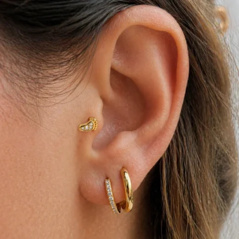 Piercing Nexa Step dorado en forma de huella colocado en la oreja con diseño minimalista y elegante