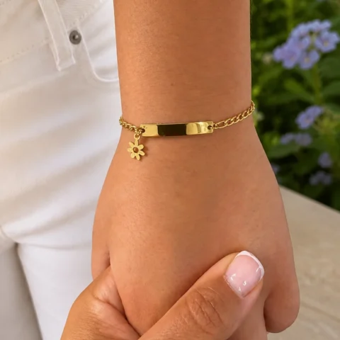 Pulsera personalizada dorada para niña con placa grabable y charm de flor puesta en muñeca